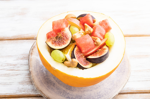 Vegetarian fruit salad of watermelon, grapes, figs, pear, orange, cashew on white wooden background. Side view, close up.