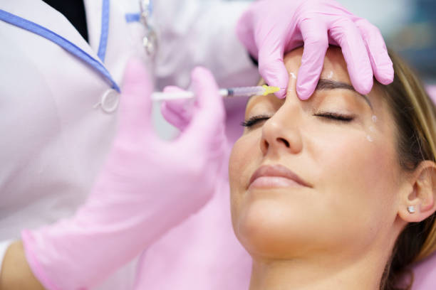 Aesthetic doctor injecting botulinum toxin into the forehead of her middle-aged patient. stock photo