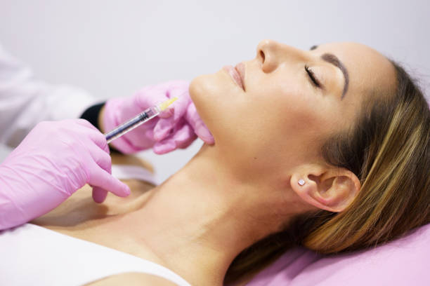 Doctor injecting hyaluronic acid into the ching of a woman as a facial rejuvenation treatment. Doctor injecting hyaluronic acid into the chin of a middle-aged woman as a facial rejuvenation treatment. chin stock pictures, royalty-free photos & images