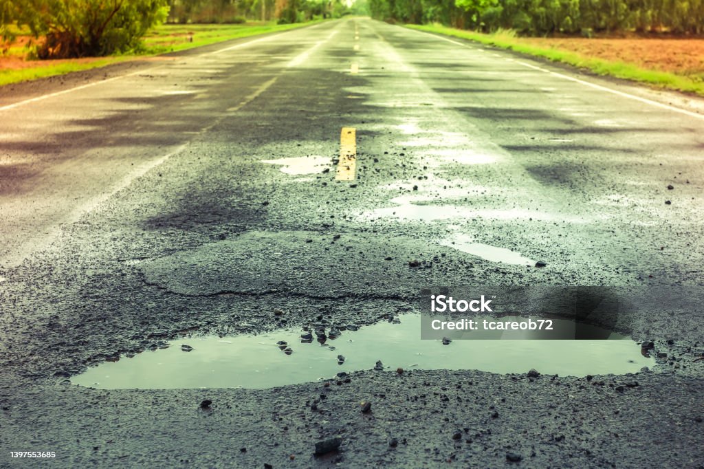 puddles on the road when it rains. puddles on the road when it rains, potholes on the highway. Sinkhole Stock Photo