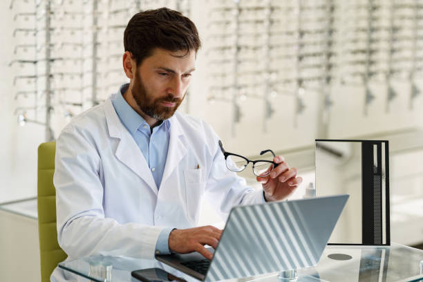 Ophthalmologist working on laptop at his workplace in optic store stock photo