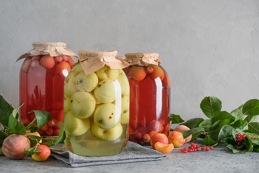 Three homemade canned fruits apple and cherry compote in large glass jars on gray table.