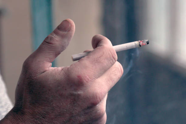 мужчина держит в руках курящую сигарету. окурок в руках курильщика - tobaco стоковые фото и изображения