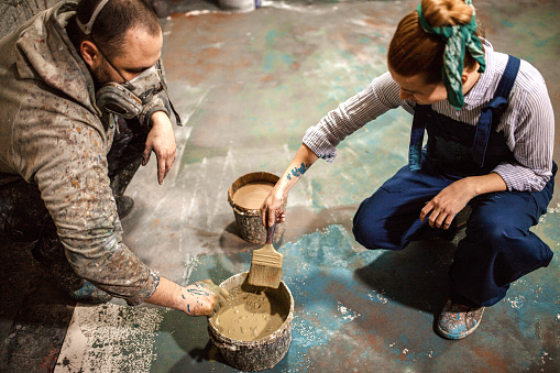 Male and female artist friends painting the floor of the studio
