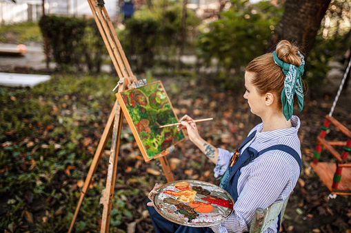 Female artist painting on canvas with paintbrush outdoors