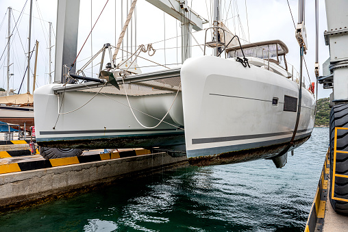 Kaş, Antalya, Turkey - April 29, 2022: Crane lifting a sailboat (catamaran) above the water on the dock for maintenance in Kaş Marina, Antalya.