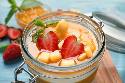 Delicious panna cotta with mango coulis and fresh fruit pieces on light blue table, closeup
