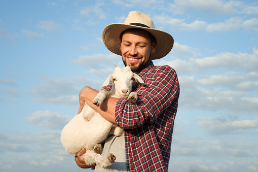 Farmer with cute goatling outdoors. Baby animal