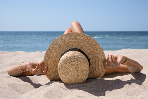 Woman with straw hat lying on sandy beach near sea