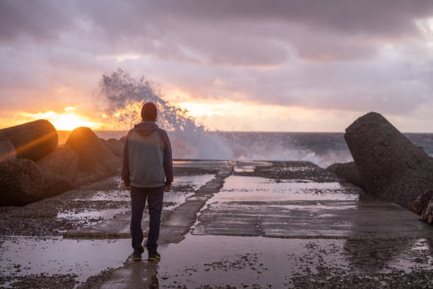 Man is thinking on the edge of  stone. Image was shot with long exposure, therefore water looks in this way. Only man was pasted and horizon was removed, other on the photo is original. Man was pasted from another image