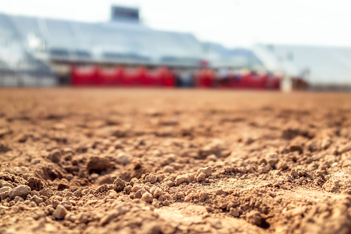 Close-up of dry dirt in the foreground, with empty grandstands in the arena defocused in the background.