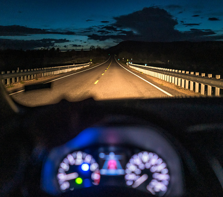 A view of the road ahead, illuminated by the car's headlights, with the instruments of the dashboard glowing, but defocused.