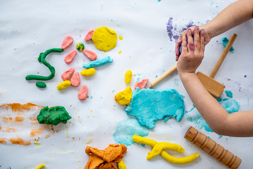 A child is seen playing with colorful plasticine in this aerial view photo.  Only their arms and hands are seen as they form the clay into various shapes.