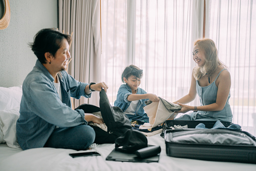 Asian family prepare luggage for holiday trips on bed in the room.