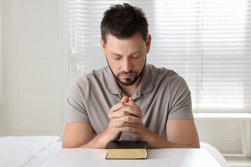 Religious man with Bible praying at home
