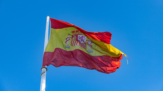 Spanish flag waving on breeze against bright blue sky