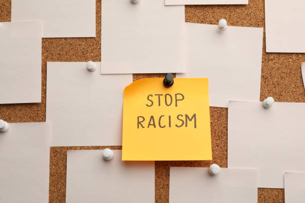 istock Yellow paper note with phrase Stop Racism among white ones attached to cork board 1397574728