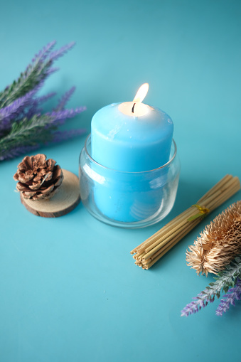 Natural candle in a glass jar and dried flowers on blue .