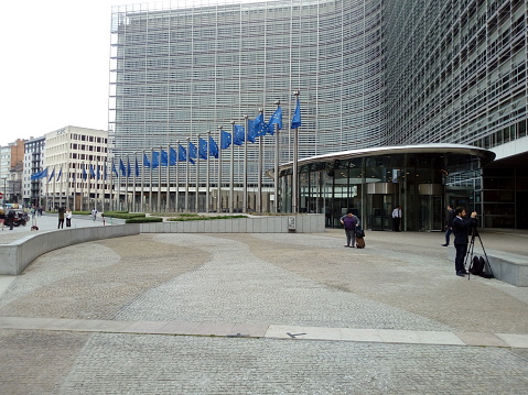 Brussels, Belgium - May 16, 2022: 4 people on the square entrance gate of the Berlaymont building. European flags in the background.