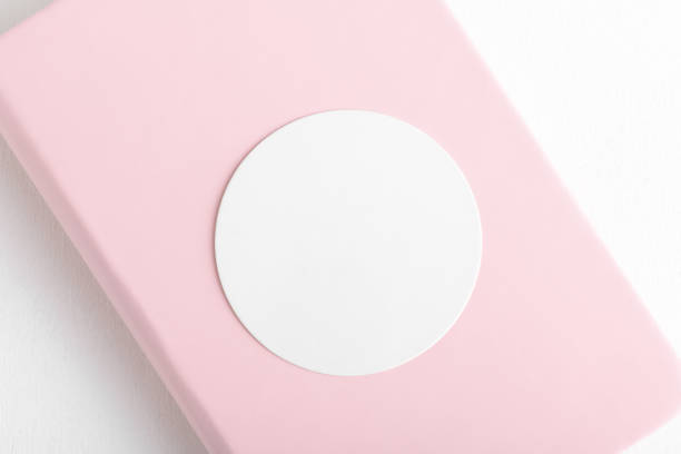 Round sticker mockup, circle white adhesive label mockup in pink book on a white background