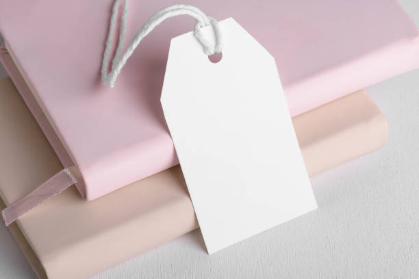 istock Rectangle white gift tag mockup with white cord, close up on beige and pink book on white background 1397578835