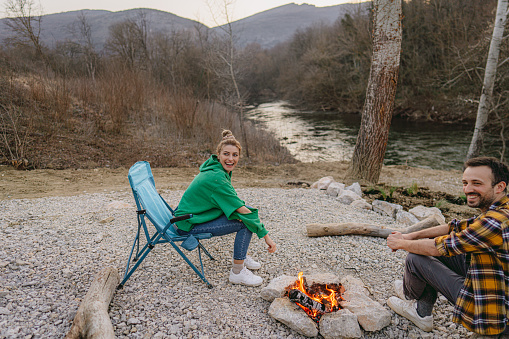 Photo of a young couple sitting by the campfire and enjoying nature together.