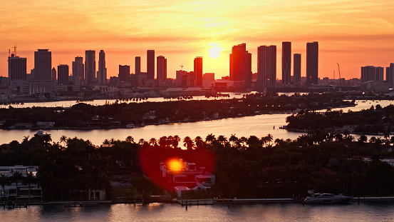 Aerial view across Biscayne Bay from Miami Beach during a beautiful sunset, looking over the Venetian Islands towards the Downtown Miami skyline silhouetted against a colorful sky. \n\nAuthorization was obtained from the FAA for this operation in restricted airspace.