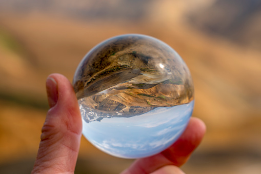 Hand holding crystal ball that reflect hot spring river at Hveradalir  geothermal area against blue sky on sunny day, Iceland