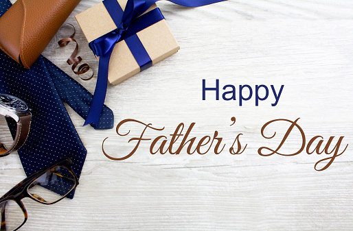 Happy Father's Day with glasses, tie, watch and gifts, on a pale rustic wooden background.