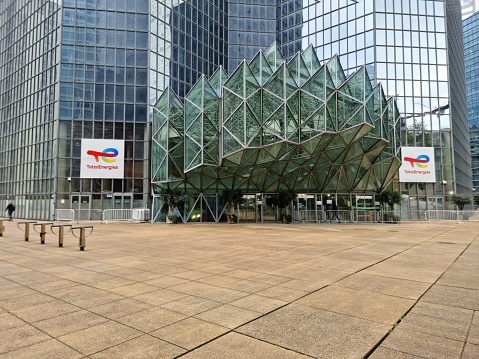 The Tour Total building now serves as headquarters for TotalEnergies. The  office building in La Défense with a height of 187 m was planned by WZMH Architects, Roger Saubot and realized between 182 and 1985. The image shows the main entrance and was captured during springtime.