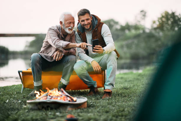 istock Happy senior father and his son using smart phone by bonfire while camping in nature. 1397595494