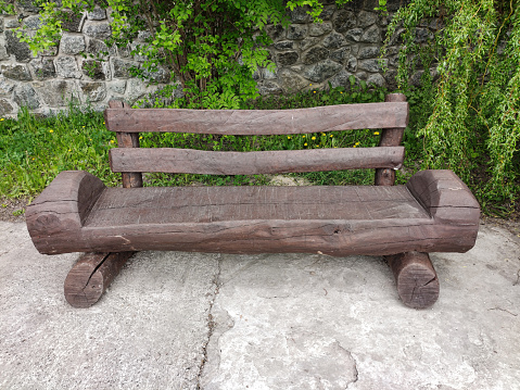 A handmade wooden bench with a painted wooden log back stands in a park