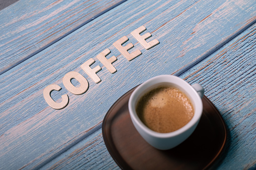 Coffee wooden text word written next to an espresso coffee served on a white cup on a blue textured background