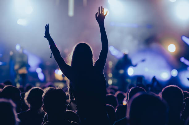 Silhouette of a woman with raised hands on a concert Silhouette of a woman in a crowd watching concert at open air music festival and enjoying. Crowd with raised hands. music festival stock pictures, royalty-free photos & images