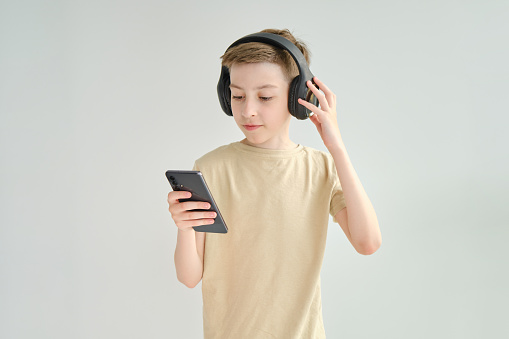 Cheerful young boy listening to the music in headphones and mobile phone isolated over blue background.