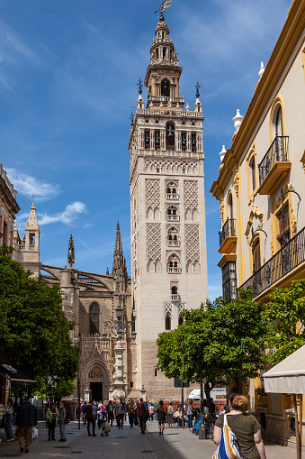 Seville, Spain - 8th April 2022. People in the street under the Giralda, the historic Moorish belltower next to the Cathedral, which was originally built as a minaret and competed in 1198.