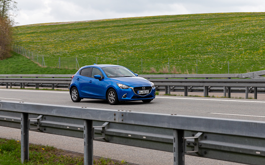 Kempten, Allgäu, Schwaben, Bavaria, Germany, may 1st 2022, a blue German Mazda2 (aka Mazda Demio) approaching on the German A7 Autobahn at Kempten - with a length of 963 km between the borders of Denmark in the north and Austria in the south, the Autobahn 7 is the longest Autobahn in Germany - the majority of the German Autobahn does not have a mandatory but only an advisory speed limit