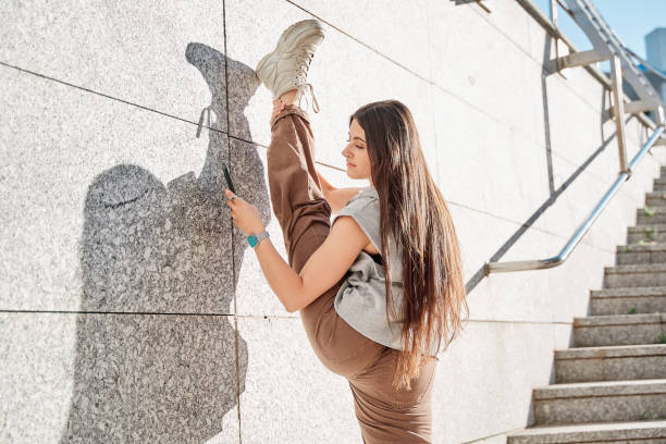 mujer adolescente levantando su pierna por encima de su cabeza en las escaleras de la ciudad usando un teléfono inteligente - female young women red hair full length fotografías e imágenes de stock