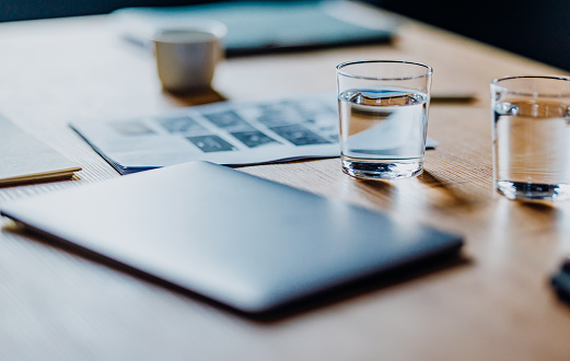 Close up photo of laptop computer on a wooden table with two glass of water and business papers.