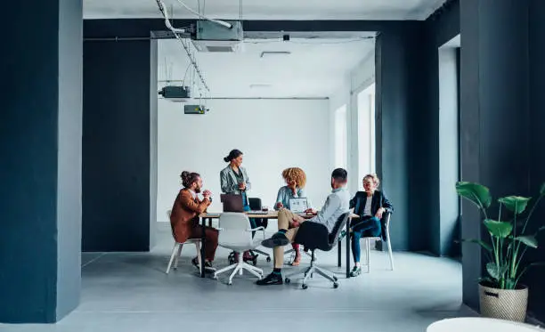 Multi ethnic team of five smiling businessman and businesswoman discussing ideas together during a casual meeting at the office desk.