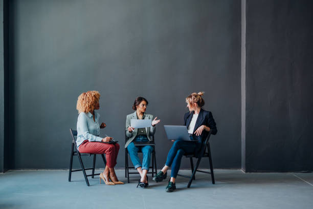 Successful team of three businesswoman working together on a laptop computer and digital tablet while sitting on a chairs in the modern office.