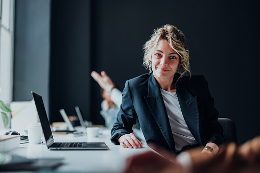 Happy businesswoman sitting at desk with laptop computer and looking at camera.