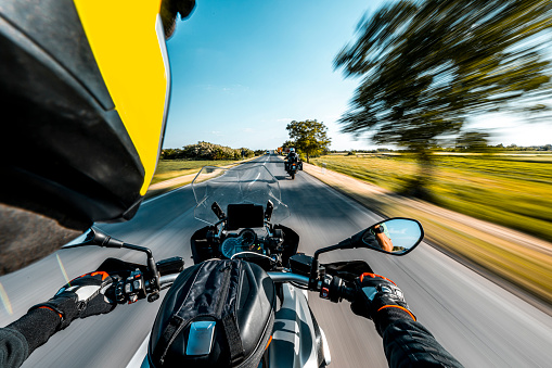 Motorcycle speeding up on an empty country road seen from over riders point of view in a beautiful nature while enjoying the adventure with his friend during one sunny spring day.