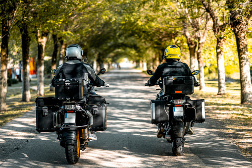 Two friends and adventure touring motorcycle riders seen on the country road going through a tunnel of trees during one sunny spring and beautiful day.