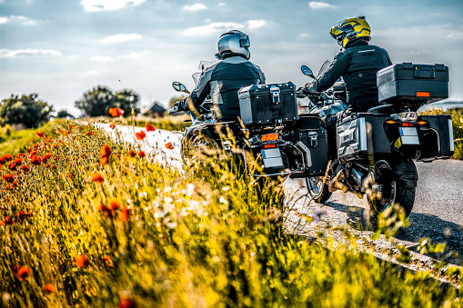 Two male off road adventure motorcycle riders seen on the road in magnificent nature with grass and flowers in a focus during one sunny spring day.