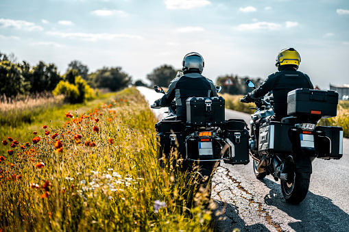 Two male adventure touring motorcycle riders seen on the road in magnificent nature with grass and flowers in a focus during one sunny weekend afternoon.