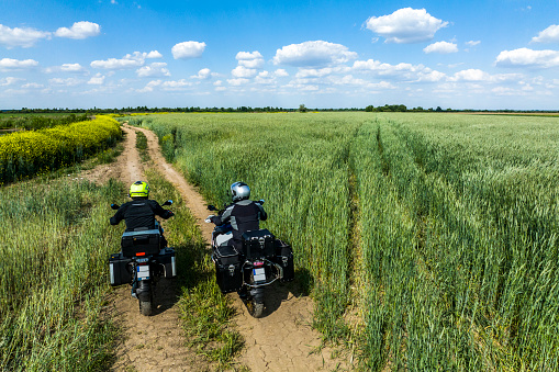 Two off road adventure motorcycle riders and friends seen from a drone point of view while enjoying the motorbike adventure in an amazing nature environment with beautiful green grass and dirt road during one sunny spring day.