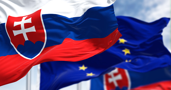 Detail of the national flag of Slovakia waving in the wind with blurred european union flag in the background on a clear day. Democracy and politics. European country. Selective focus.