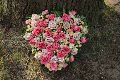 A sympathy flower arrangement in a heart shape, pink and purple roses