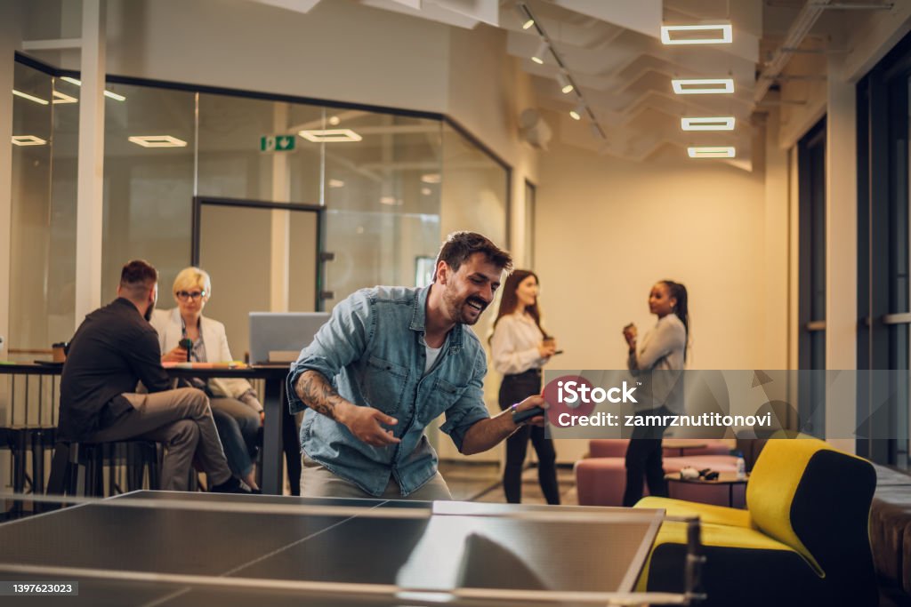 Young people playing table tennis in the office at work Games between employees during a work break. Colleagues are playing table tennis at work. Having some fun at the office. Portrait of a business man in casual clothes playing ping pong. Table Tennis Stock Photo
